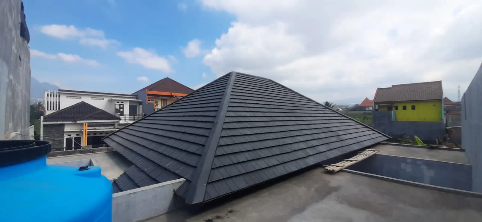 Atap genteng beton dengan tandon air biru di bidang dak beton di sekelilingnya