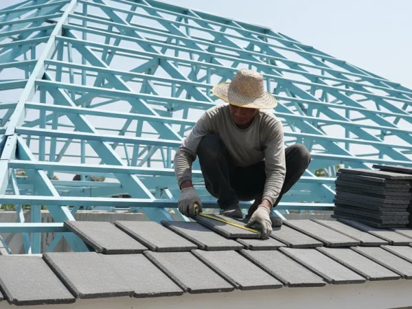 Pekerja berjongkok di atas bidang atap genteng beton yang sedang dipasang
